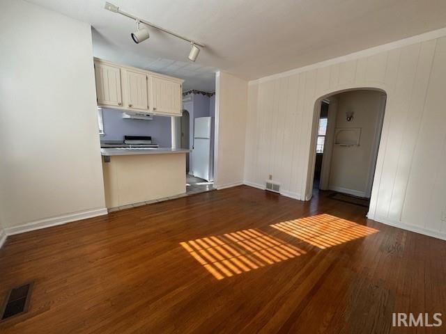 kitchen with dark hardwood / wood-style flooring, rail lighting, white fridge, and wooden walls