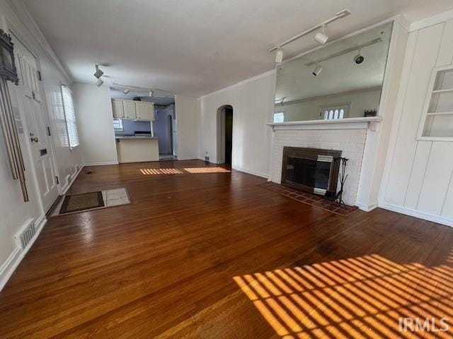 unfurnished living room with rail lighting, a fireplace, ornamental molding, and dark wood-type flooring