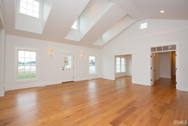 unfurnished living room featuring light hardwood / wood-style floors, high vaulted ceiling, and a skylight