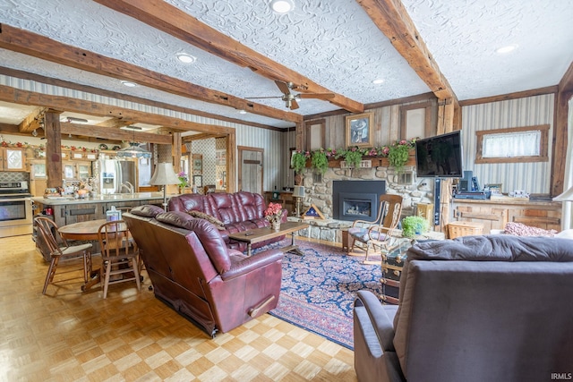 living room with ceiling fan, a fireplace, a textured ceiling, beamed ceiling, and light parquet flooring