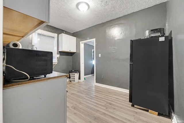 kitchen featuring black refrigerator, a textured ceiling, light wood-type flooring, and white cabinets