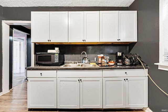 kitchen featuring white cabinetry, sink, light hardwood / wood-style flooring, backsplash, and a textured ceiling