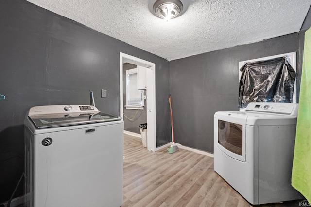 clothes washing area featuring a textured ceiling, light hardwood / wood-style floors, and washing machine and clothes dryer