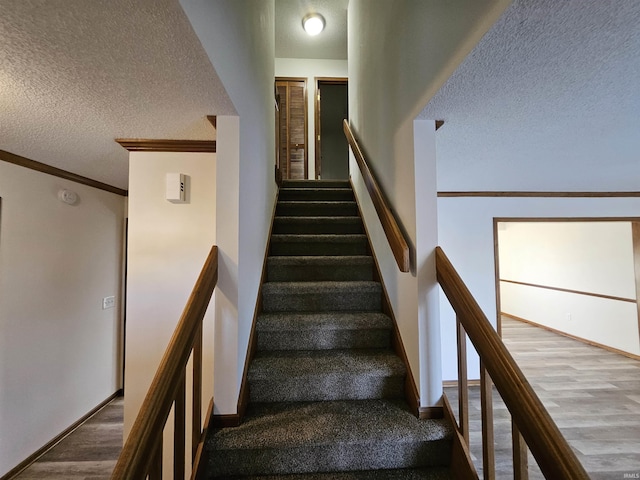 stairway with hardwood / wood-style floors, a textured ceiling, and crown molding