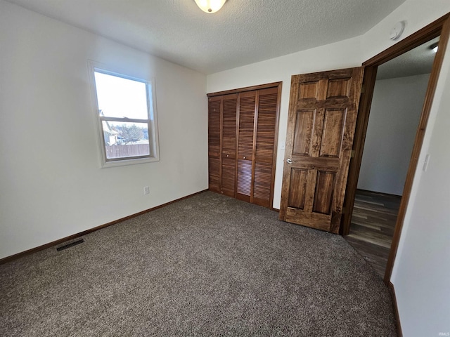 unfurnished bedroom featuring a textured ceiling, dark carpet, and a closet