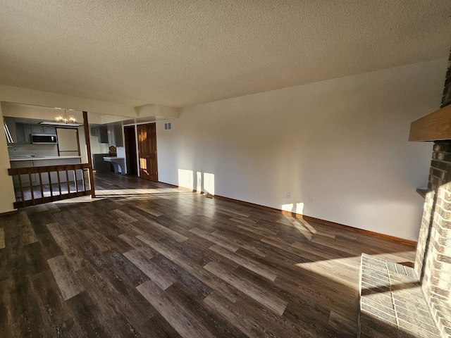 unfurnished living room with a textured ceiling, a brick fireplace, and dark wood-type flooring