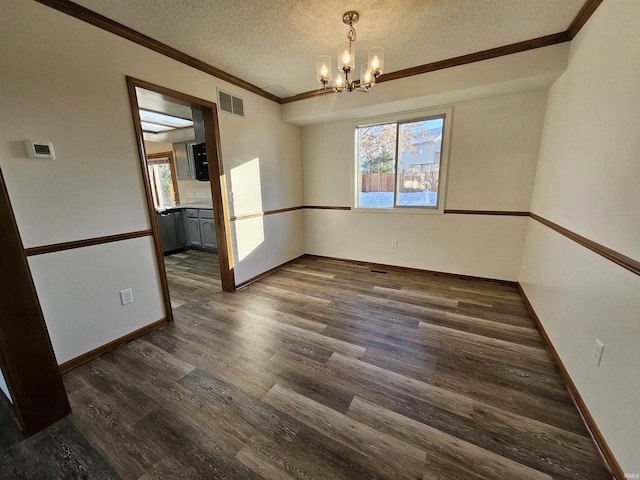 spare room with a notable chandelier, dark hardwood / wood-style floors, ornamental molding, and a textured ceiling