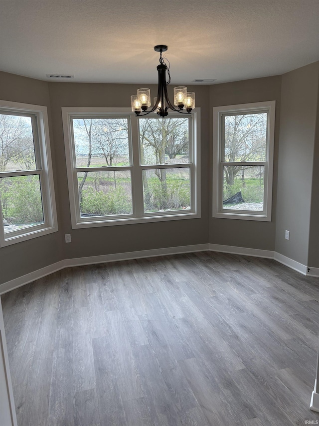 unfurnished dining area featuring visible vents, baseboards, wood finished floors, and a notable chandelier