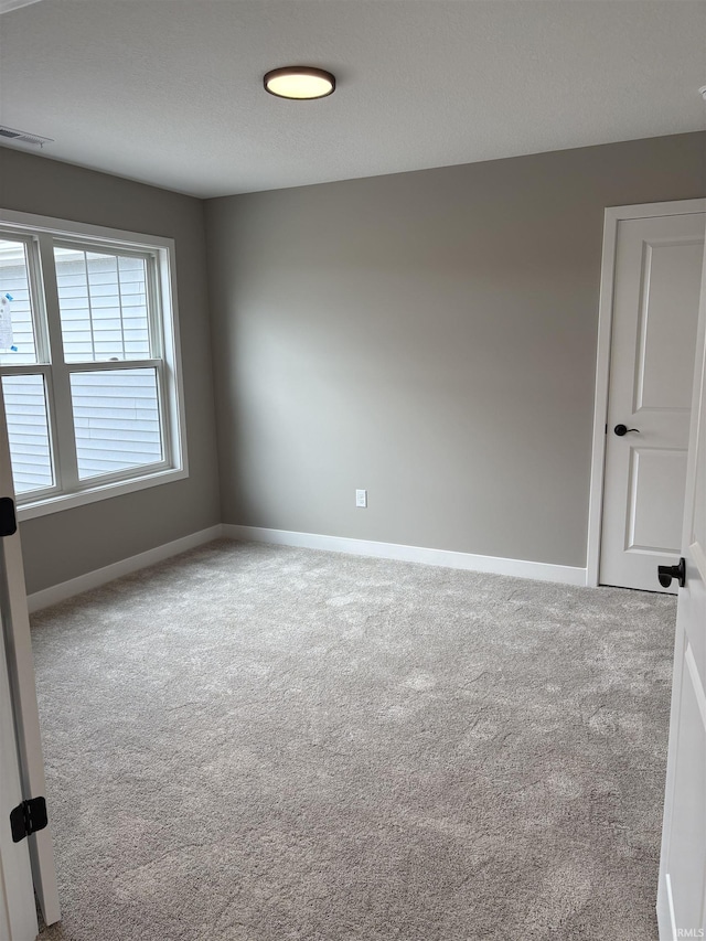 spare room featuring carpet floors, visible vents, and baseboards