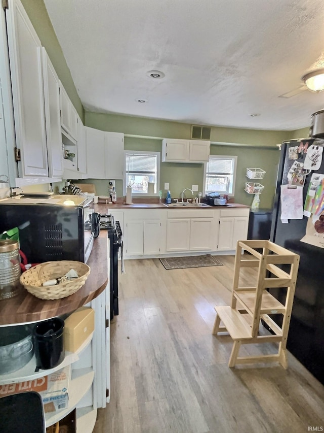 kitchen featuring black appliances, white cabinetry, sink, and light hardwood / wood-style floors