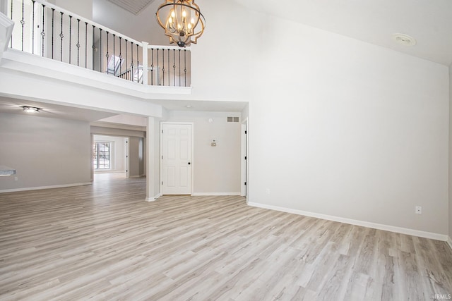 unfurnished living room with light wood-type flooring, a towering ceiling, and an inviting chandelier