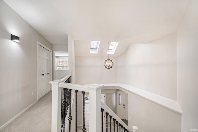 hallway with light colored carpet, a notable chandelier, and vaulted ceiling with skylight