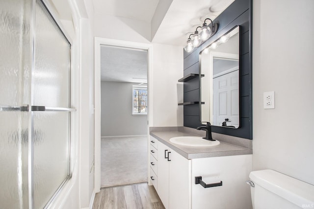 full bathroom with combined bath / shower with glass door, wood-type flooring, vanity, and toilet