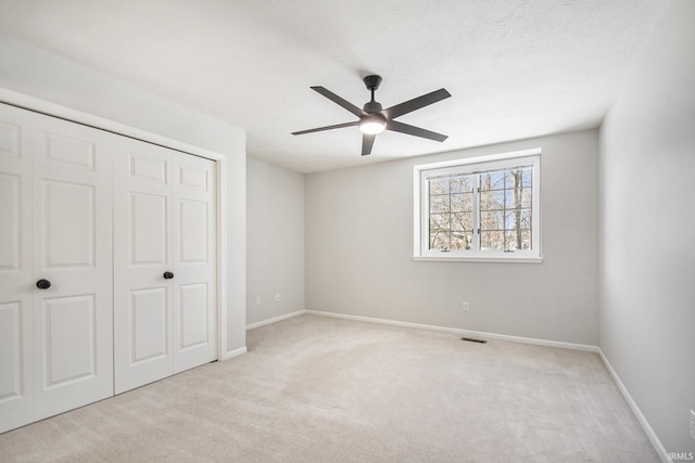 unfurnished bedroom with ceiling fan, a closet, light carpet, and a textured ceiling