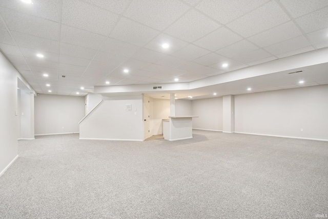 basement with a paneled ceiling and light colored carpet