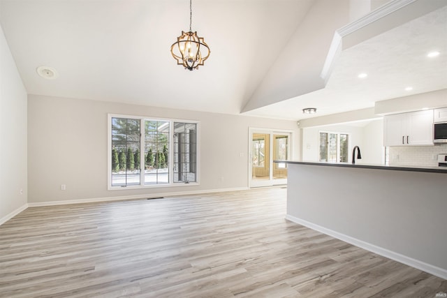 unfurnished living room featuring an inviting chandelier, sink, high vaulted ceiling, and light hardwood / wood-style flooring