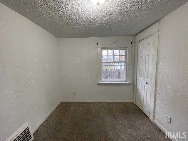 spare room featuring dark carpet and a textured ceiling