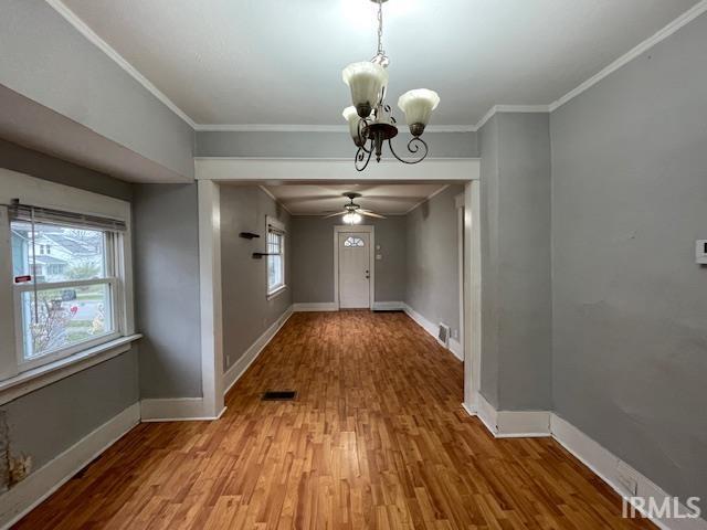 unfurnished dining area featuring wood-type flooring, ceiling fan with notable chandelier, and crown molding