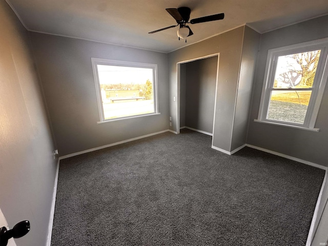 unfurnished bedroom featuring ceiling fan, multiple windows, a closet, and dark colored carpet