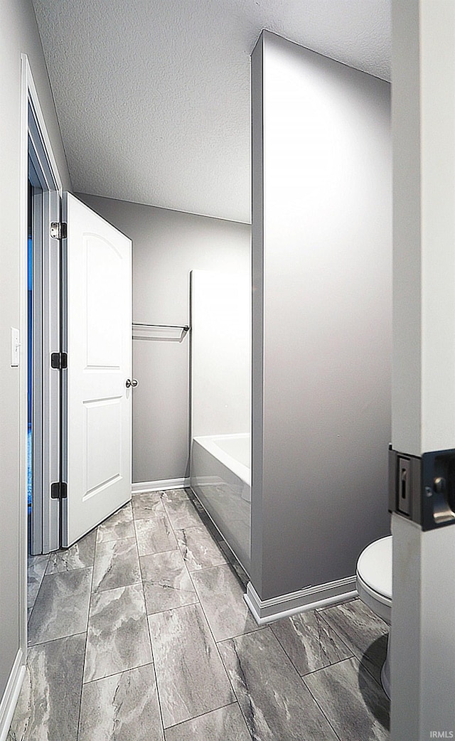 bathroom with a textured ceiling, toilet, and a bathing tub