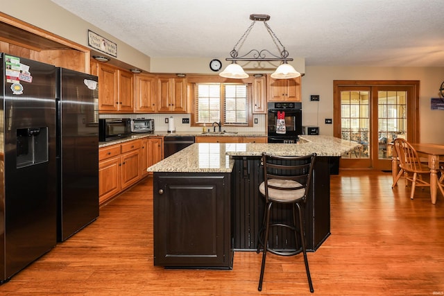 kitchen with black appliances, a center island, sink, and light hardwood / wood-style flooring