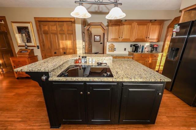 kitchen featuring fridge with ice dispenser, dark hardwood / wood-style floors, pendant lighting, a kitchen island with sink, and black electric stovetop