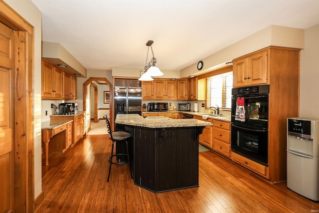 kitchen featuring light stone counters, dark wood-type flooring, sink, black appliances, and a kitchen island