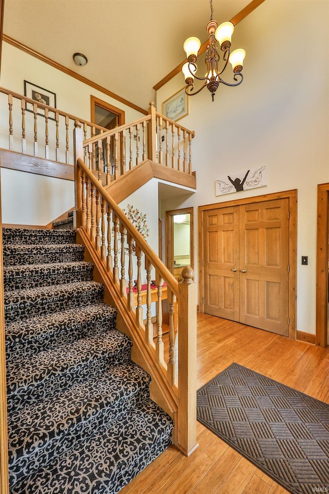 staircase featuring hardwood / wood-style floors, ornamental molding, a notable chandelier, and a high ceiling