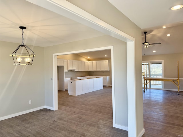 kitchen with white cabinetry, hanging light fixtures, ceiling fan with notable chandelier, and dark hardwood / wood-style flooring