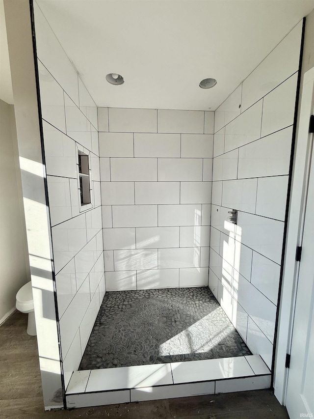 bathroom with wood-type flooring, tiled shower, and toilet