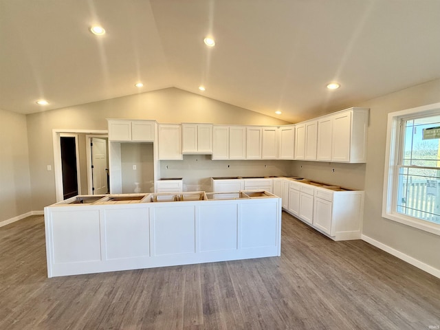 kitchen featuring hardwood / wood-style flooring, lofted ceiling, a kitchen island, and white cabinets