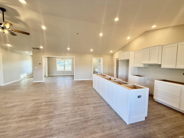 kitchen with vaulted ceiling, a kitchen island, white cabinetry, ceiling fan, and light hardwood / wood-style floors