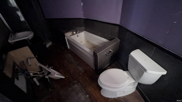 bathroom with a washtub, hardwood / wood-style floors, toilet, and tile walls