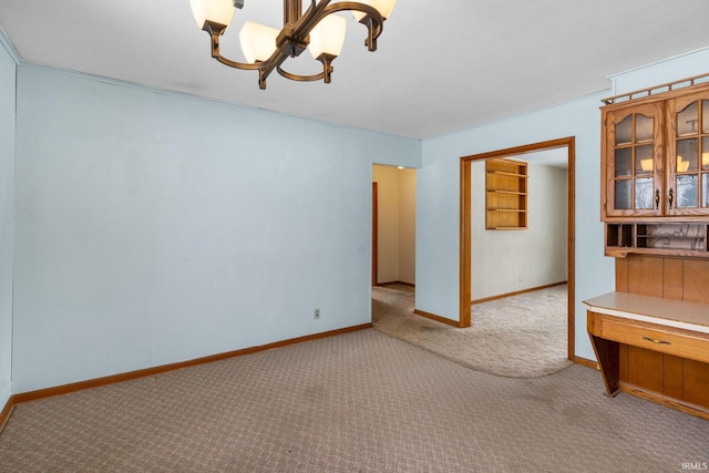 spare room featuring light carpet, ornamental molding, and a notable chandelier