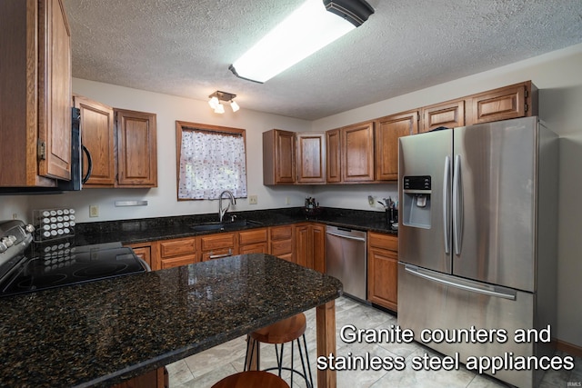 kitchen featuring a textured ceiling, dark stone countertops, sink, and appliances with stainless steel finishes