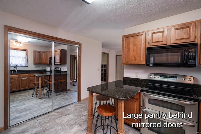 kitchen with sink, dark stone countertops, stainless steel electric range oven, a textured ceiling, and a kitchen bar