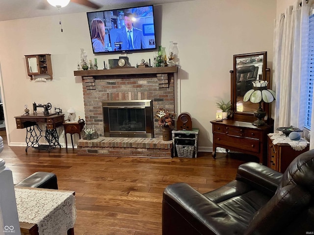 living room featuring ceiling fan, wood-type flooring, and a brick fireplace