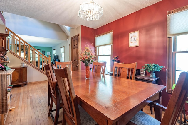 dining space with a notable chandelier, light wood-type flooring, and a textured ceiling