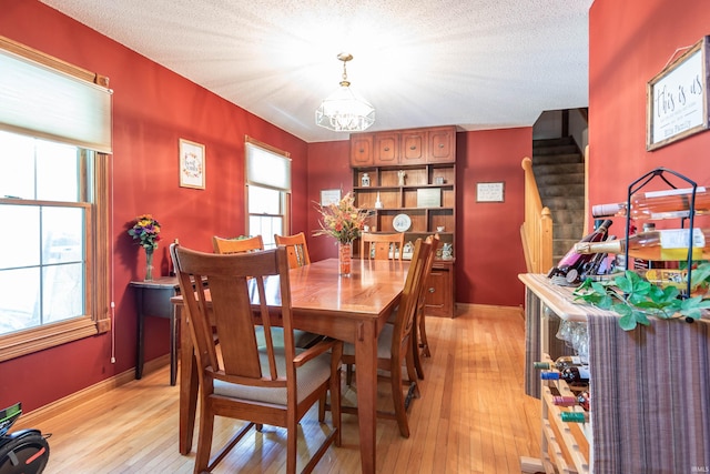 dining area with an inviting chandelier, a textured ceiling, and light wood-type flooring