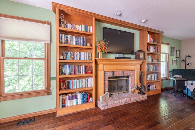 living room with a textured ceiling, dark hardwood / wood-style floors, and a brick fireplace