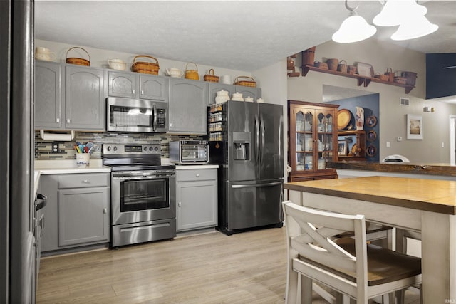 kitchen featuring stainless steel appliances, backsplash, pendant lighting, light hardwood / wood-style floors, and gray cabinets