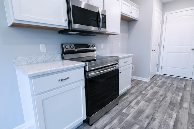 kitchen with white cabinets, light hardwood / wood-style floors, light stone countertops, and appliances with stainless steel finishes