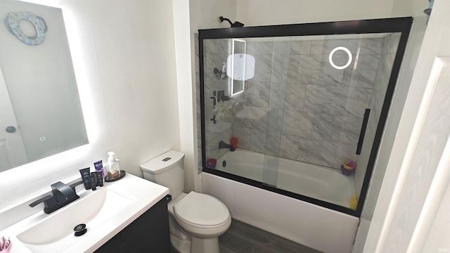 full bathroom with vanity, hardwood / wood-style flooring, toilet, and bath / shower combo with glass door