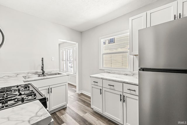 kitchen featuring stainless steel refrigerator, white cabinetry, sink, light hardwood / wood-style floors, and a textured ceiling