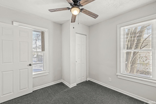 unfurnished bedroom with dark colored carpet, ceiling fan, a closet, and multiple windows