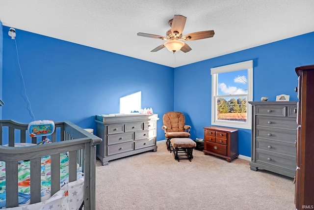 bedroom with a textured ceiling, ceiling fan, light carpet, and a crib