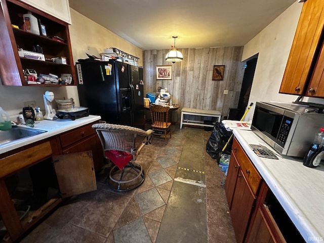 kitchen with black fridge, sink, wood walls, and decorative light fixtures