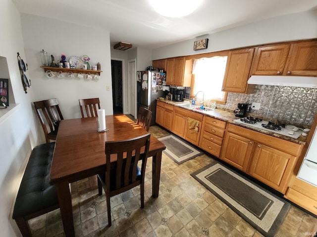 kitchen featuring white gas stovetop, backsplash, sink, light stone countertops, and stainless steel refrigerator