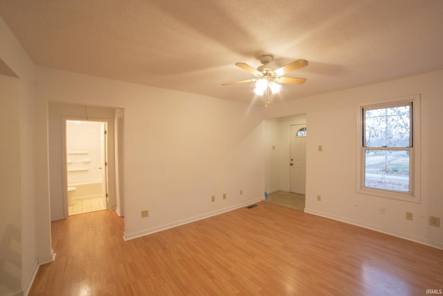 empty room with visible vents, a ceiling fan, a textured ceiling, light wood finished floors, and baseboards