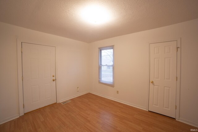 unfurnished room with visible vents, baseboards, a textured ceiling, and light wood finished floors